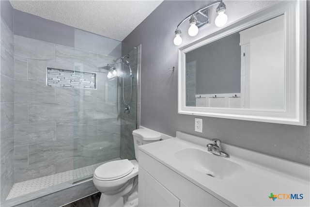 bathroom featuring a tile shower, vanity, a textured ceiling, and toilet