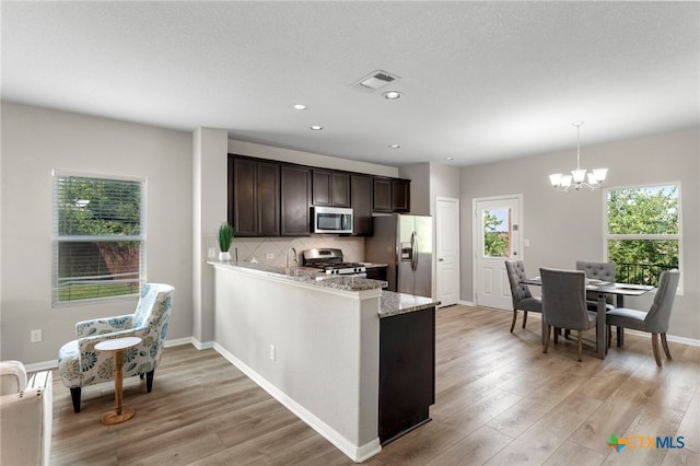 480 Waterloo Dr, Kyle, TX 78640 - kitchen with stainless steel appliances, a chandelier, dark brown cabinetry, light wood-style floors, and recessed lighting
