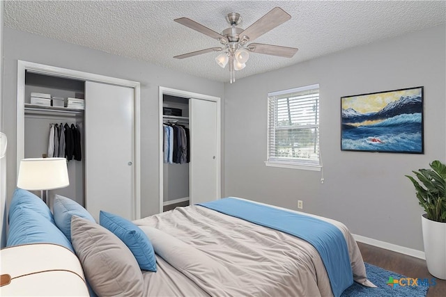 bedroom with a textured ceiling, wood finished floors, a ceiling fan, baseboards, and multiple closets