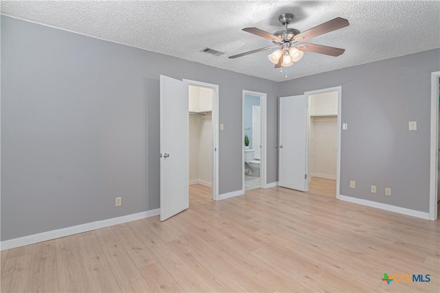 unfurnished bedroom featuring light wood-style flooring, visible vents, baseboards, a closet, and a walk in closet