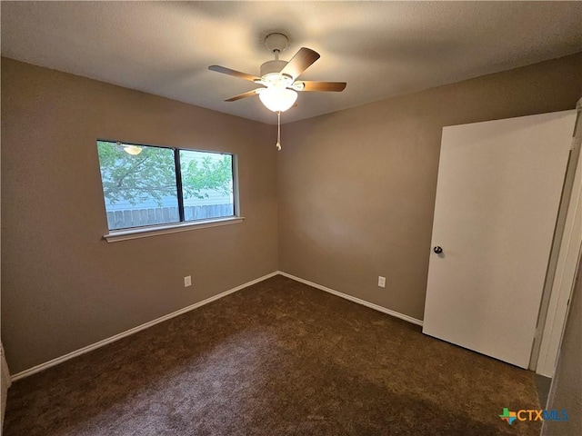 empty room featuring dark colored carpet, a ceiling fan, and baseboards