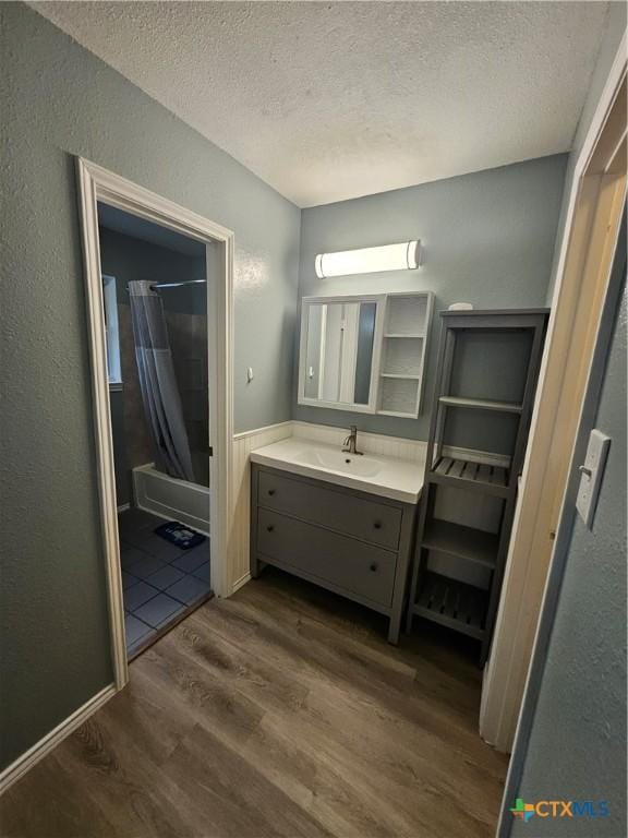 bathroom with a textured ceiling, wood finished floors, vanity, a textured wall, and shower / bathtub combination with curtain