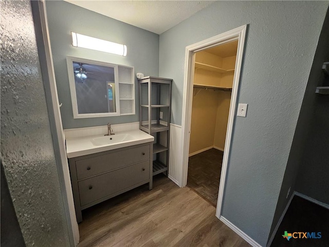 bathroom featuring ceiling fan, a spacious closet, wood finished floors, and vanity
