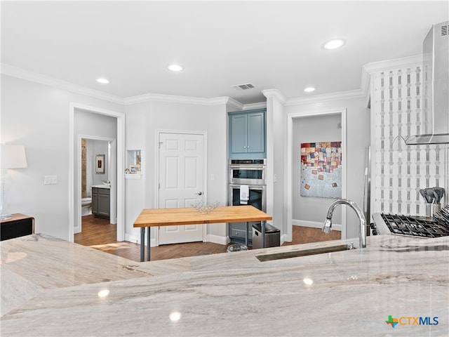 kitchen featuring light stone countertops, wall chimney exhaust hood, ornamental molding, stainless steel double oven, and sink