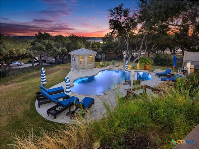 pool at dusk with a lawn and an outdoor structure