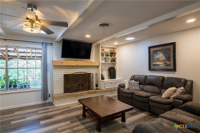 living room with built in features, hardwood / wood-style floors, a brick fireplace, beamed ceiling, and ceiling fan