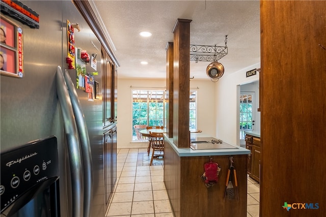 kitchen with black electric stovetop, a center island, a textured ceiling, light tile patterned flooring, and stainless steel fridge