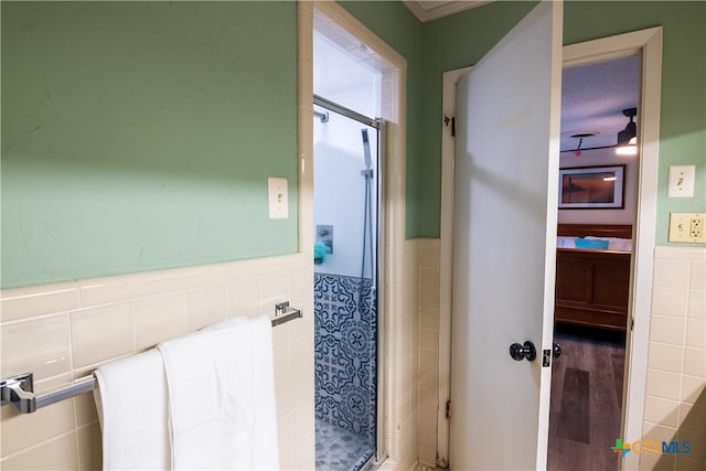 bathroom featuring tile walls, hardwood / wood-style flooring, and a shower with shower door