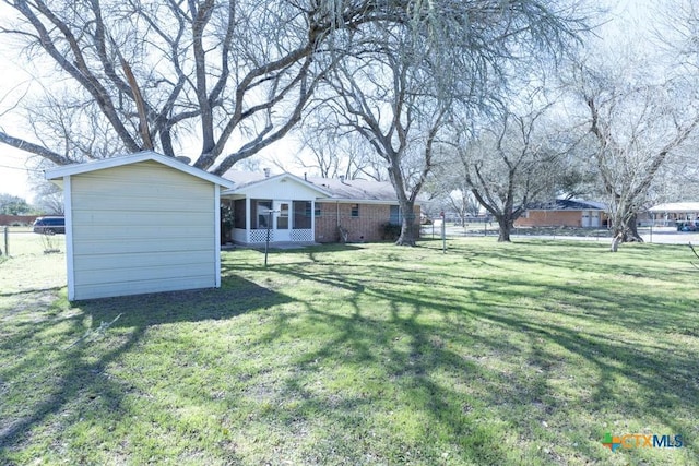 view of yard featuring an outbuilding, a storage shed, fence, and a sunroom