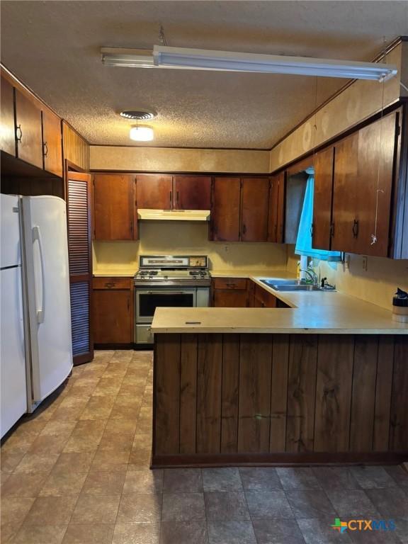 302 E Heard St, Ganado, TX 77962 - kitchen featuring freestanding refrigerator, stainless steel range, a peninsula, light countertops, and under cabinet range hood
