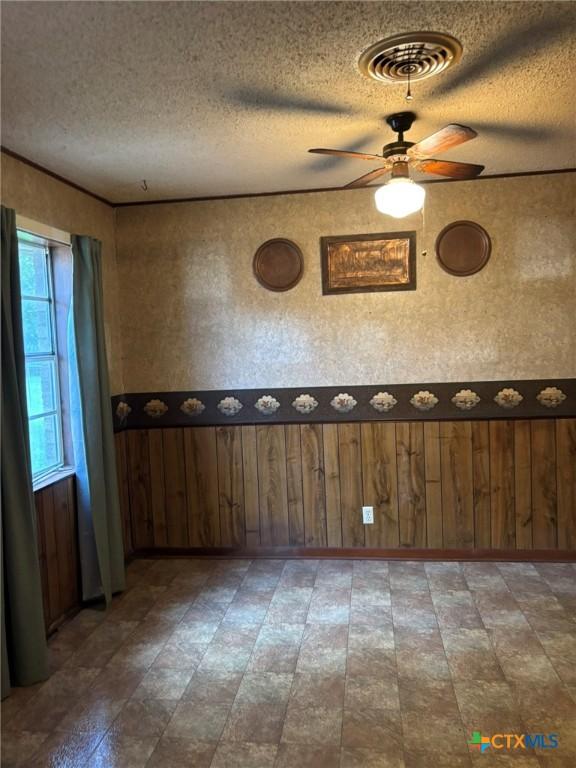 302 E Heard St, Ganado, TX 77962 - empty room featuring a textured ceiling, a ceiling fan, wooden walls, and a wainscoted wall