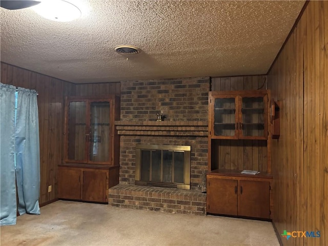 302 E Heard St, Ganado, TX 77962 - unfurnished living room featuring wooden walls, light carpet, a brick fireplace, and a textured ceiling