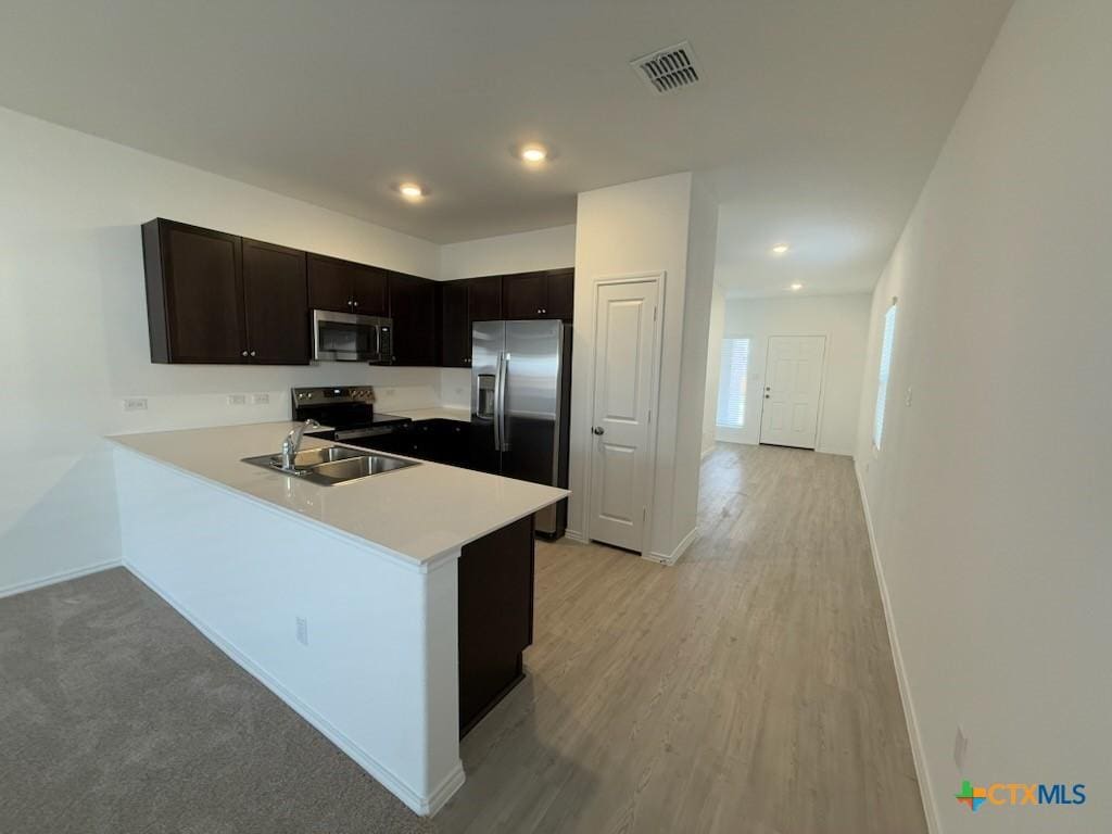 kitchen with kitchen peninsula, sink, stainless steel appliances, and light hardwood / wood-style flooring