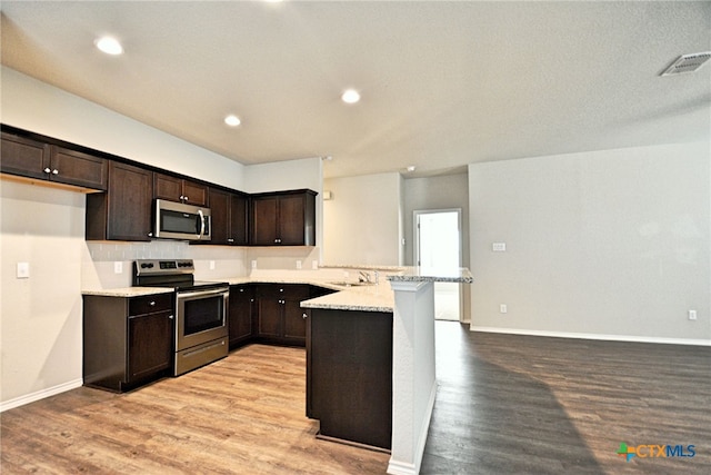 475 Autumn Leaf Dr, New Braunfels, TX 78130 - kitchen featuring stainless steel appliances, a peninsula, dark brown cabinets, light wood-style floors, and recessed lighting