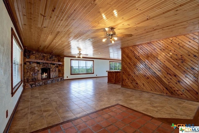 unfurnished living room with wooden walls, dark tile patterned flooring, ceiling fan, wood ceiling, and a stone fireplace