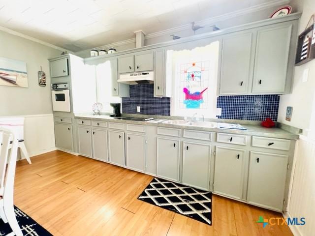 kitchen with tasteful backsplash, ornamental molding, cooktop, white oven, and light wood-type flooring