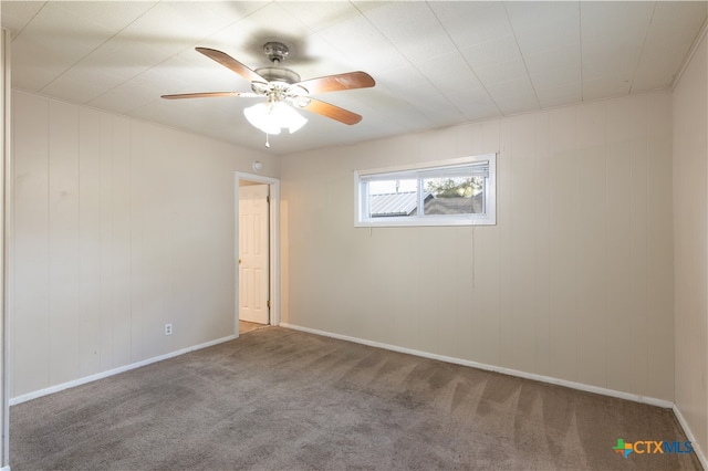 empty room with carpet flooring, wooden walls, and ceiling fan