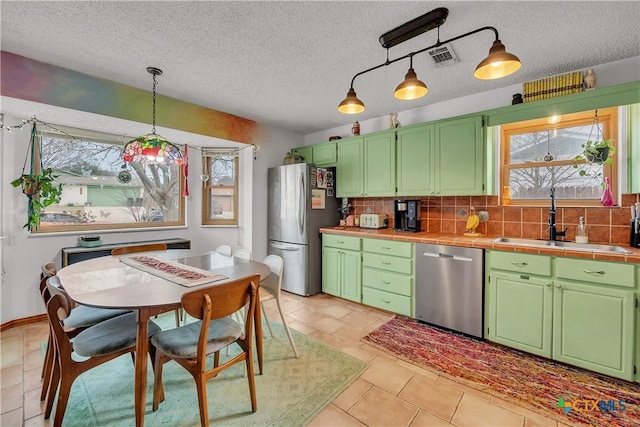 kitchen with tile counters, stainless steel appliances, sink, hanging light fixtures, and backsplash