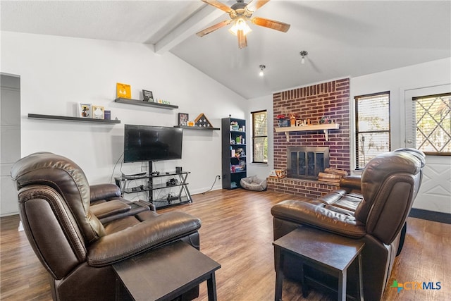 living room with lofted ceiling with beams, ceiling fan, wood-type flooring, and a brick fireplace