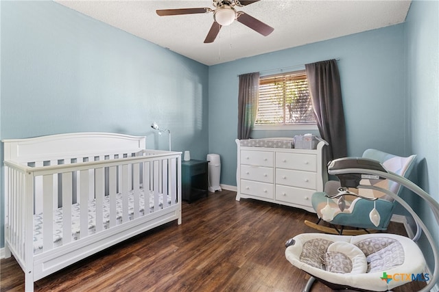 bedroom with a textured ceiling, ceiling fan, a nursery area, and dark hardwood / wood-style floors