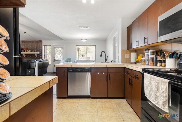 kitchen with kitchen peninsula, appliances with stainless steel finishes, light tile patterned flooring, and sink