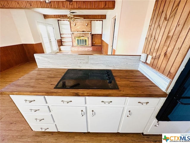 kitchen with white cabinets, black stovetop, butcher block counters, and ceiling fan