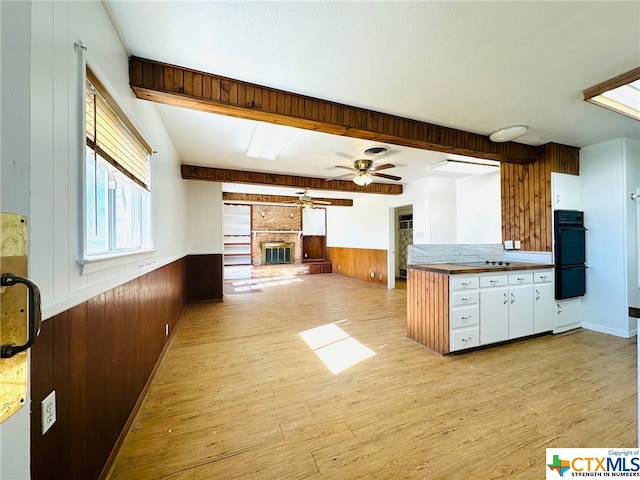 kitchen featuring white cabinets, wooden walls, a brick fireplace, and light hardwood / wood-style flooring