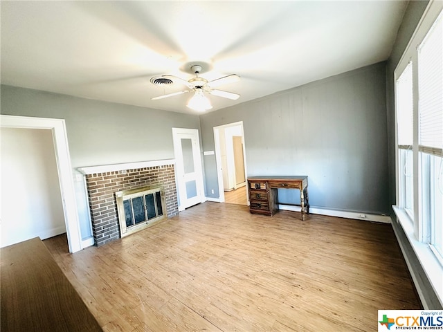 unfurnished living room with light wood-type flooring, a wealth of natural light, ceiling fan, and a brick fireplace