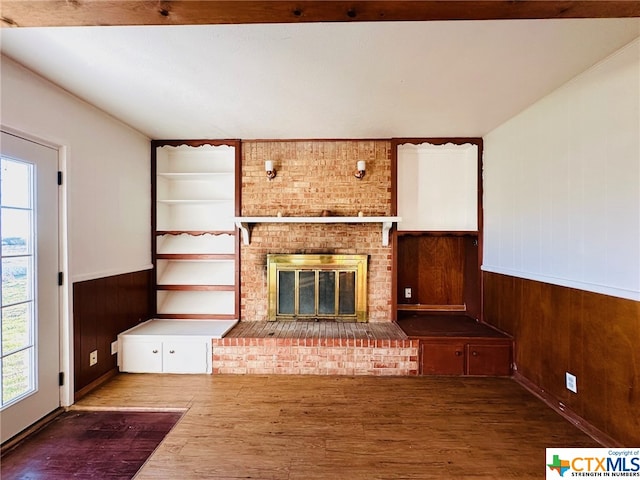 unfurnished living room with wooden walls, wood-type flooring, and a fireplace