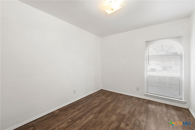 spare room featuring baseboards and dark wood-type flooring