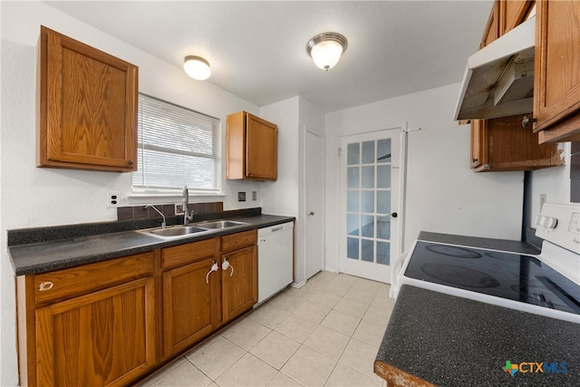 kitchen with brown cabinets, under cabinet range hood, a sink, dark countertops, and white appliances