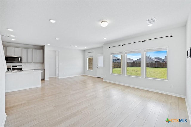 unfurnished living room with light wood-type flooring, visible vents, a sink, recessed lighting, and baseboards