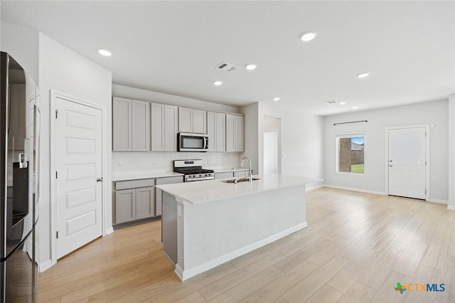 kitchen with tasteful backsplash, gray cabinetry, appliances with stainless steel finishes, light wood-style floors, and a sink