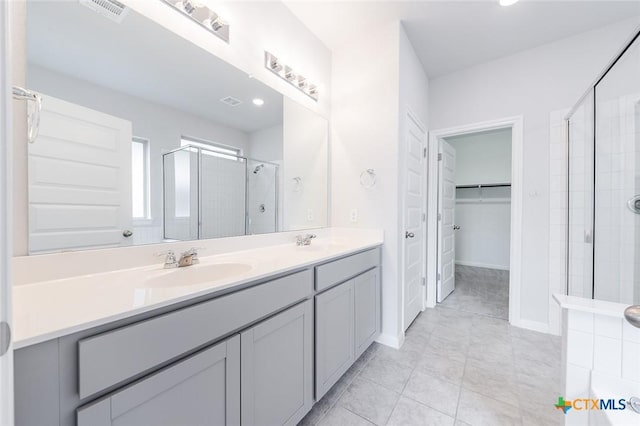 bathroom with visible vents, a walk in closet, a sink, a shower stall, and double vanity