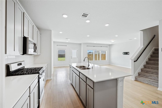 kitchen with visible vents, gray cabinetry, a sink, light wood-style floors, and appliances with stainless steel finishes