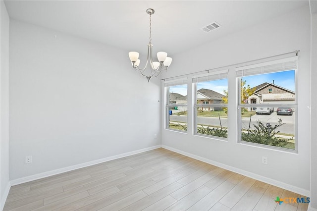 spare room with visible vents, baseboards, a notable chandelier, and wood finished floors