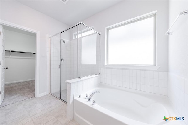 full bath featuring a shower stall, a spacious closet, a bath, and baseboards