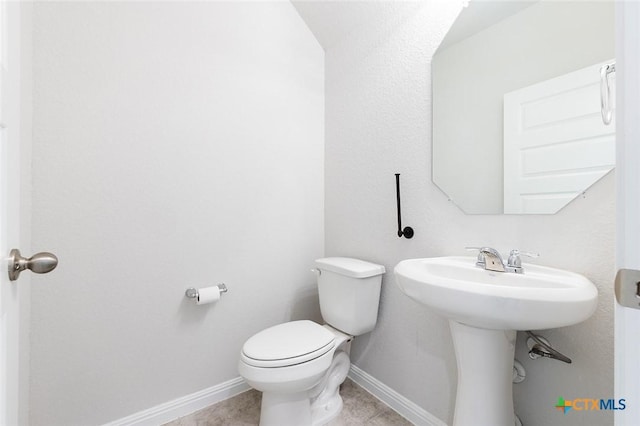 half bath featuring a sink, baseboards, toilet, and tile patterned flooring