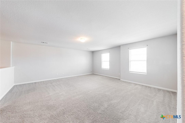 carpeted spare room featuring baseboards, visible vents, and a textured ceiling