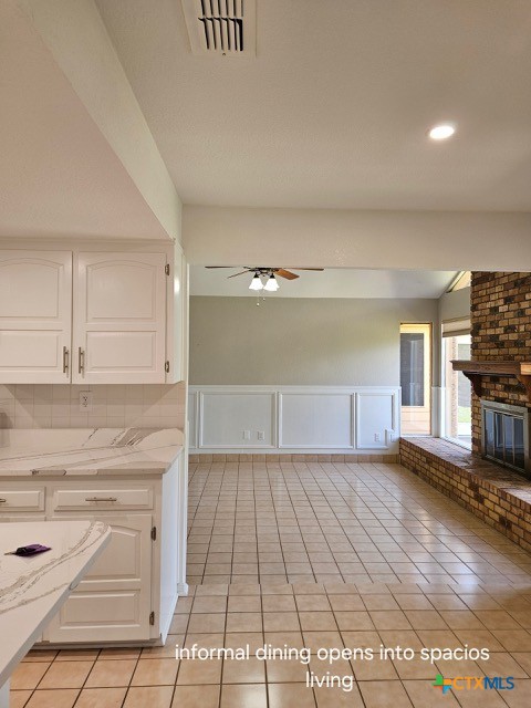 kitchen featuring light tile patterned floors, white cabinets, visible vents, a brick fireplace, and ceiling fan