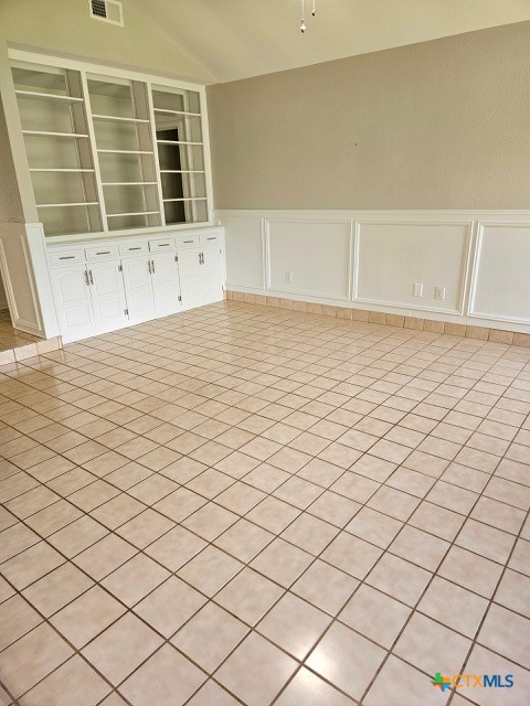 empty room featuring a decorative wall, vaulted ceiling, wainscoting, and visible vents