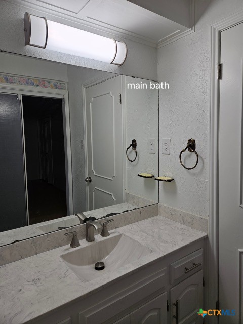 bathroom with crown molding, vanity, and a textured wall