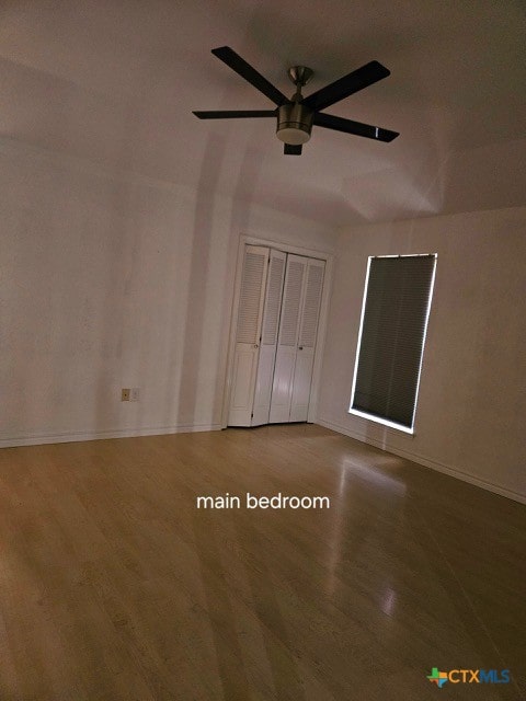 unfurnished bedroom with a ceiling fan, wood finished floors, baseboards, and a closet