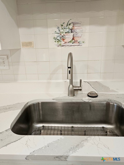 interior details featuring a sink, backsplash, and light stone counters