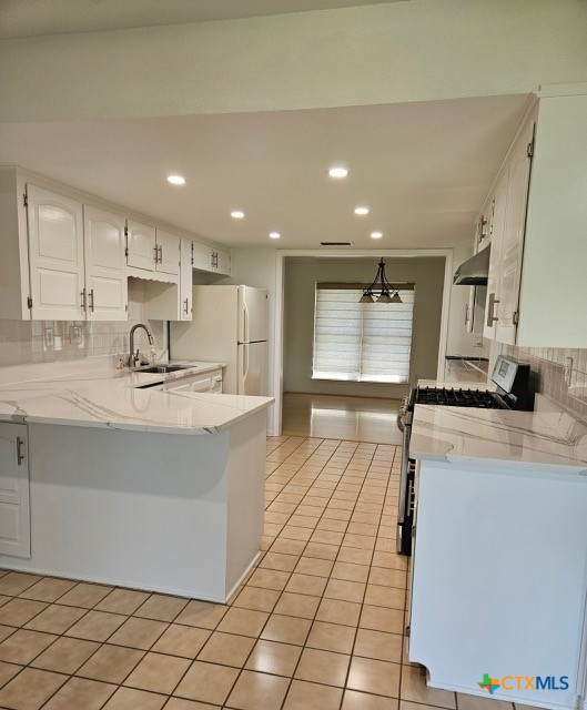 kitchen with a peninsula, wall chimney range hood, white cabinets, a sink, and decorative backsplash