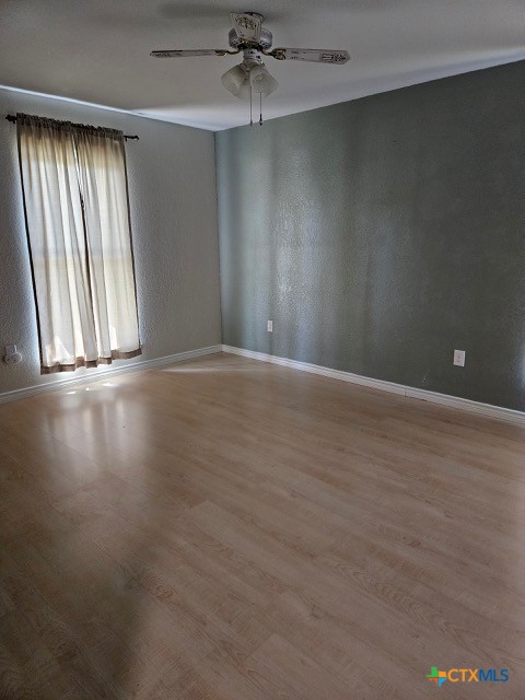 empty room with a textured wall, ceiling fan, baseboards, and wood finished floors