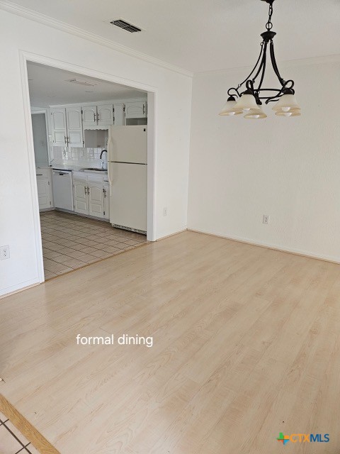unfurnished dining area with a sink, ornamental molding, light wood-type flooring, and visible vents