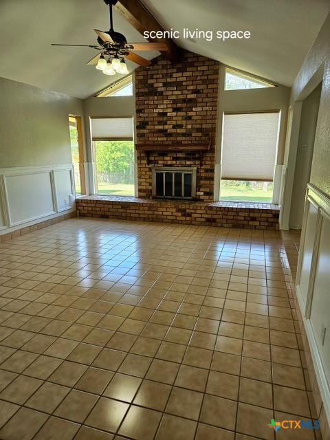 unfurnished living room featuring a decorative wall, ceiling fan, vaulted ceiling with beams, a brick fireplace, and tile patterned floors