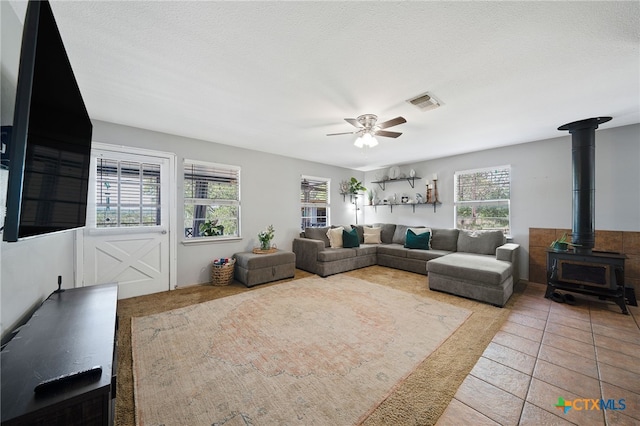 tiled living room featuring visible vents, a wood stove, and a ceiling fan