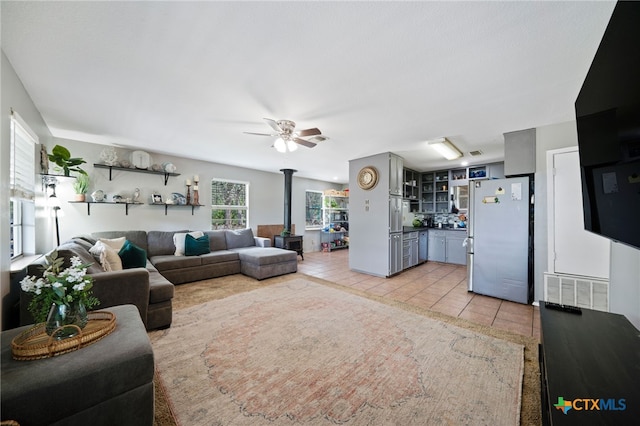 living room with ceiling fan, light tile patterned floors, and a wood stove